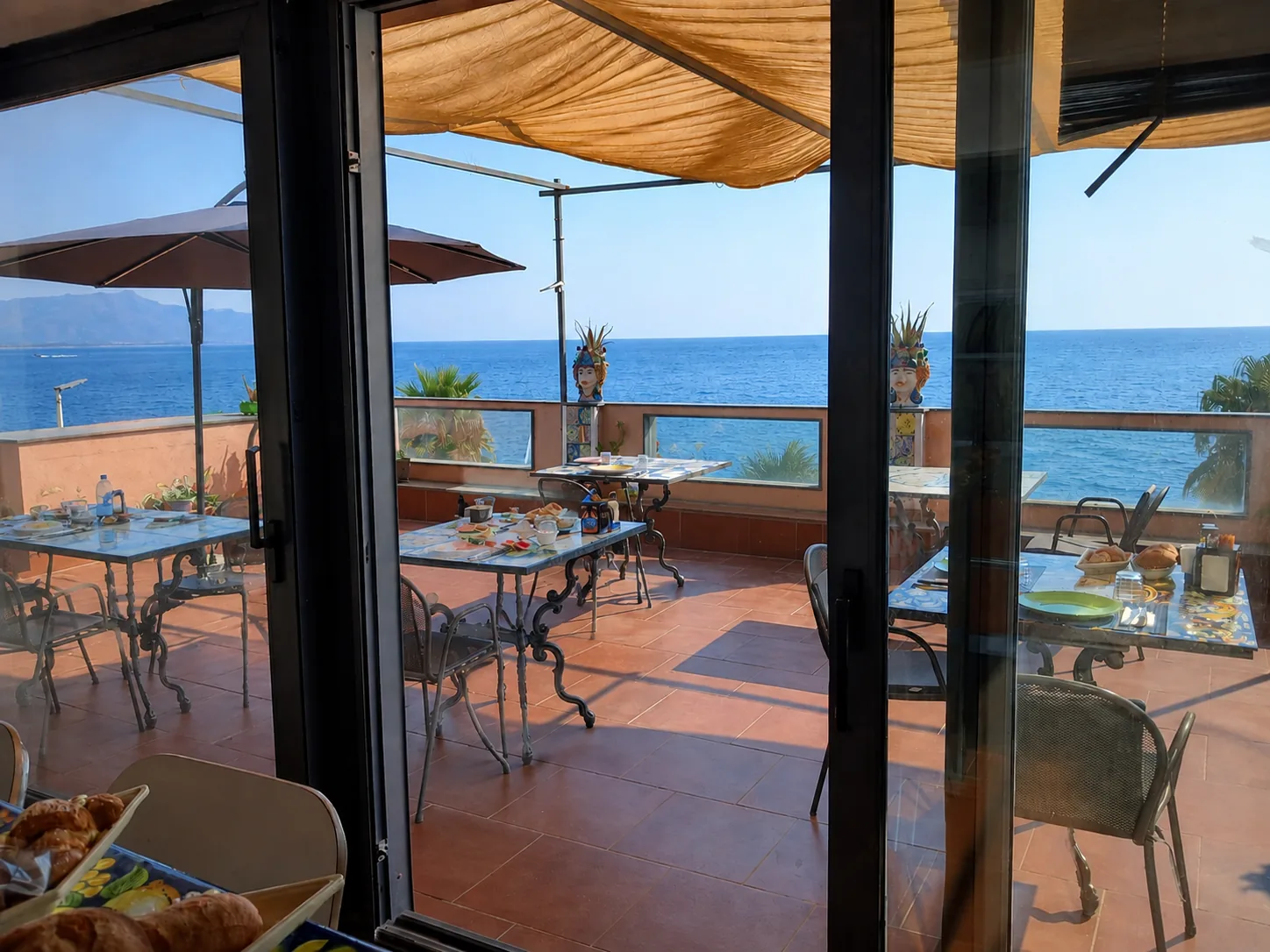 La terrazza di Mar dei Poeti attraverso la vetrata, con i tavoli apparecchiati e il mare davanti